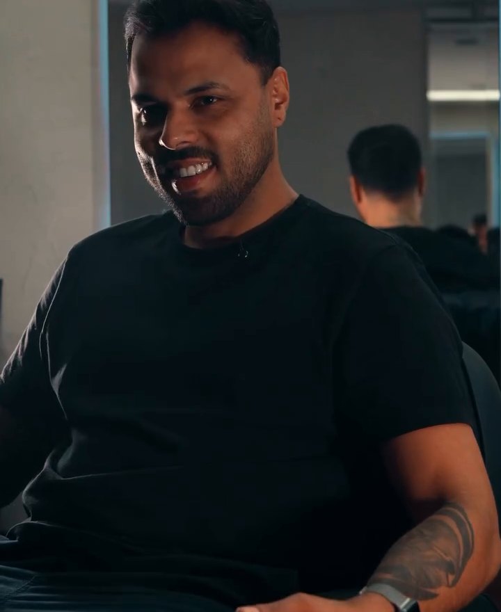 Átila Fernandes sorrindo, de camiseta preta, no salão da SAAT
