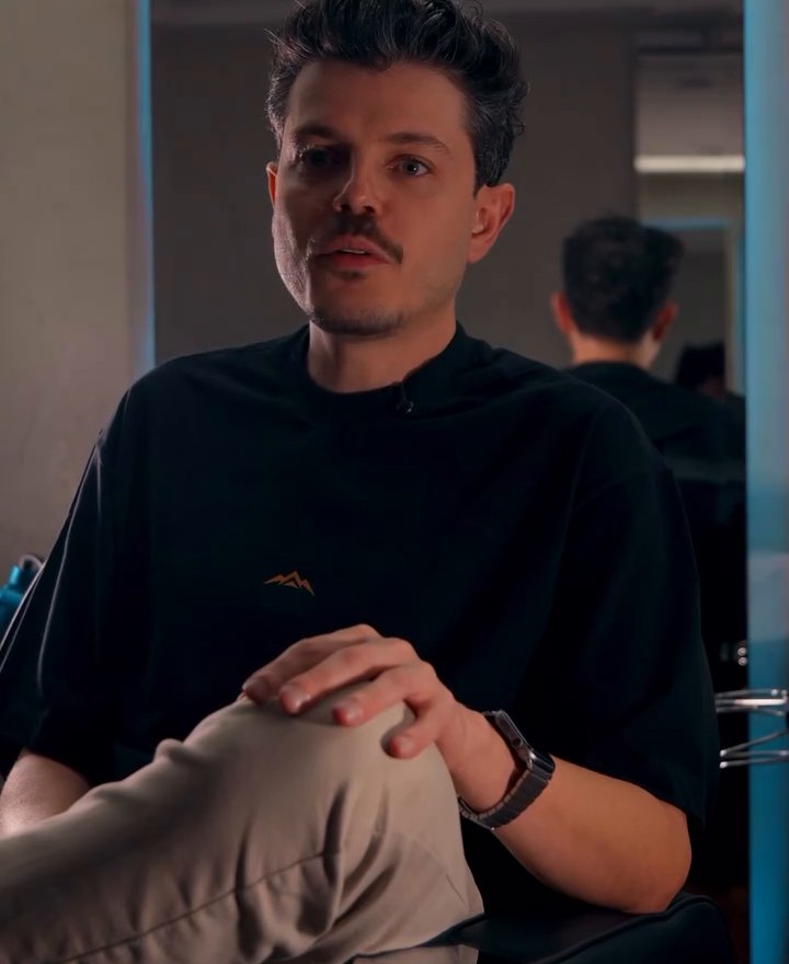 Lucas Sadi sentado, de camiseta preta, no salão da SAAT